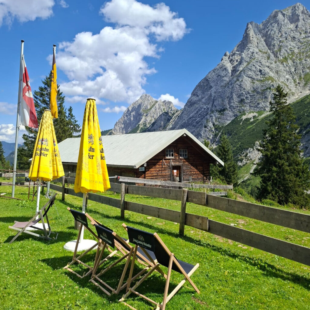 Panorama-Aussicht von der Terrasse der Füssener Hütte auf die grün bewaldeten Hänge und schroffen Gipfel der Tannheimer Alpen unter blauem Himmel © Radio Alpenwelle CE2607